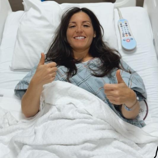 Young Leadership Council member Marisa Stachelski in a hospital bed giving 2-thumbs up