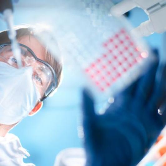 Scientist wearing goggles and a mask in a lab researching with blood samples and a pipette