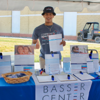 Man smiling and holding a flyer behind a Basser Center booth